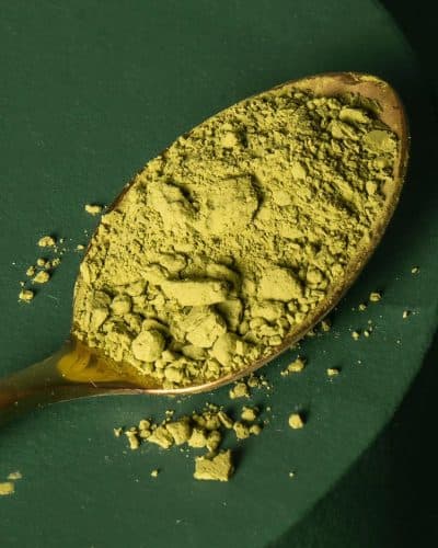 Gros plan sur une cuillère dorée remplie de poudre de matcha vert vif